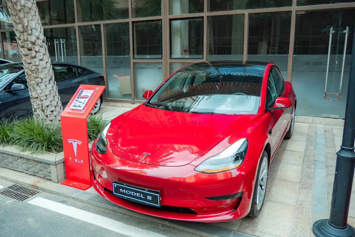 閃亮的紅色特斯拉Model 3停在人行道上，風挡玻璃上有反射。