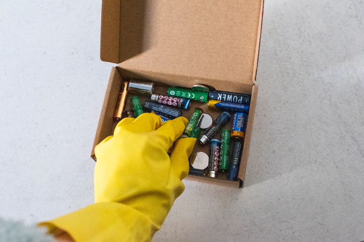 Yellow-gloved hand handling used batteries for safe recycling.