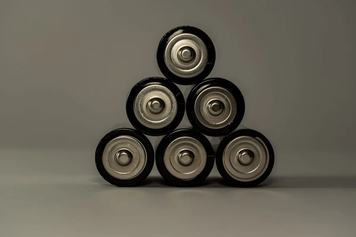 Zes zwarte batterijen liggen in een piramide op een grijze ondergrond, met de ronde zilveren pluspolen duidelijk naar de camera gericht.